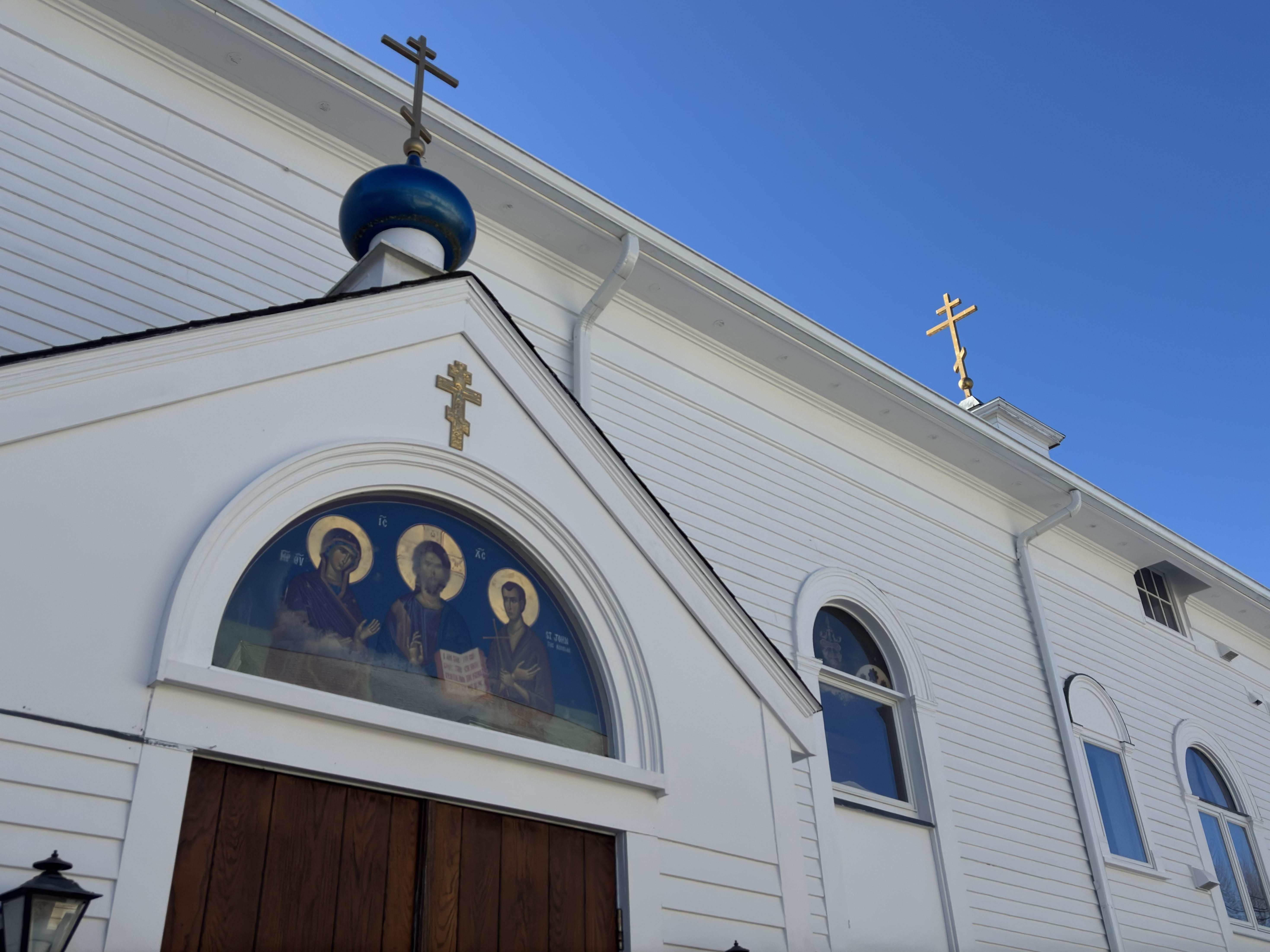 A low-angle shot of the white-painted exterior of St. John the Russian Orthodox Church under a clear blue sky.